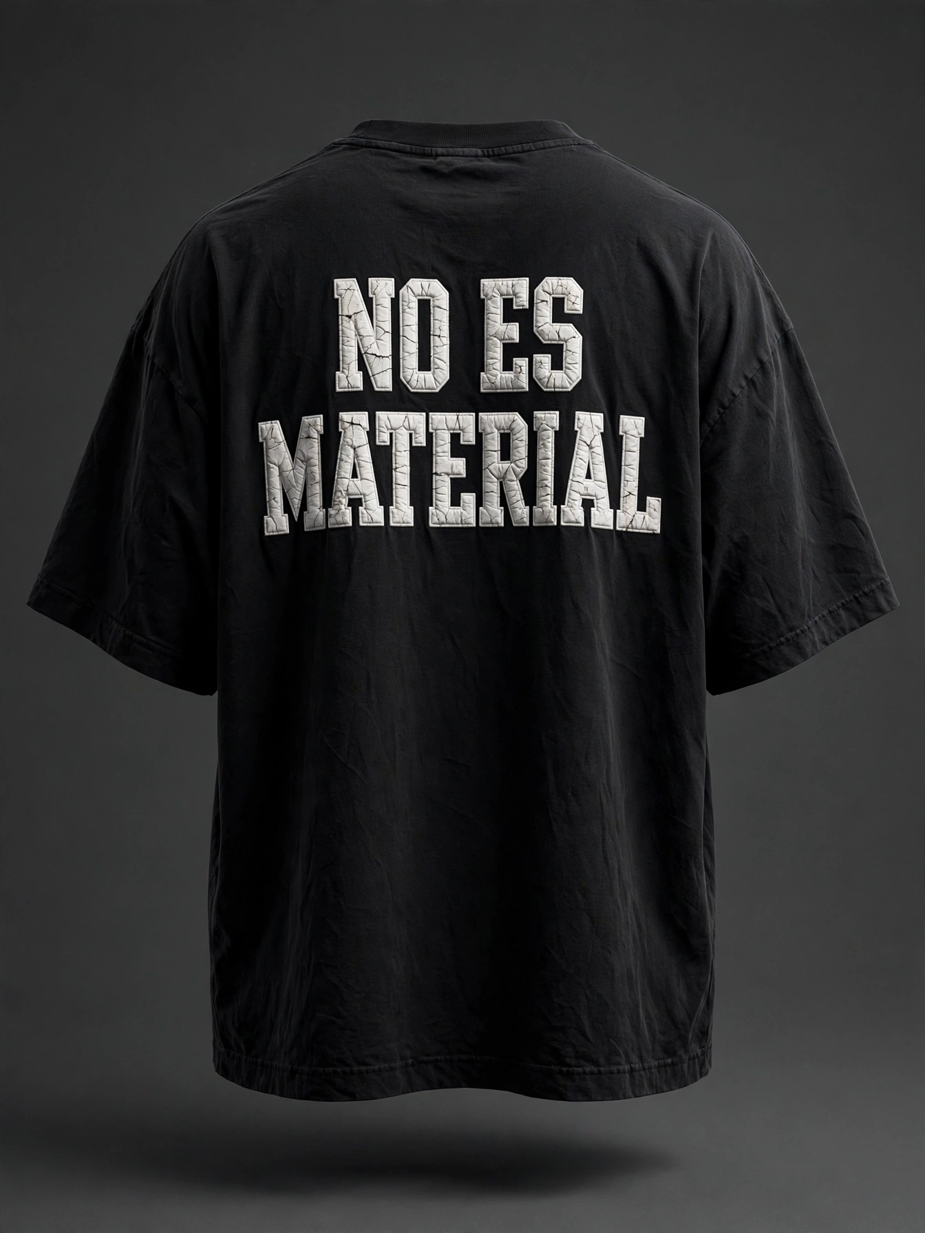 Back of an oversized black T-shirt with the No Es Material message in cracked lettering